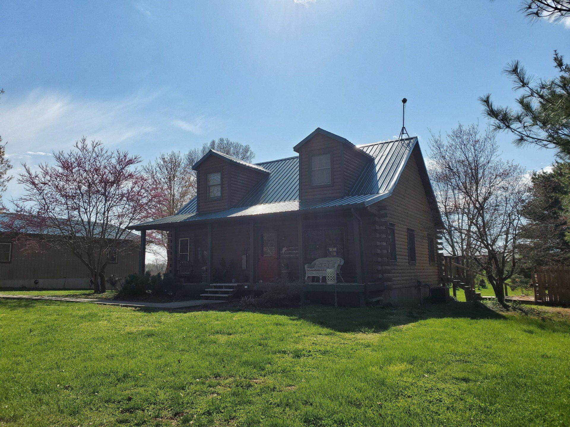 A house with a metal roof is sitting in the middle of a lush green field.