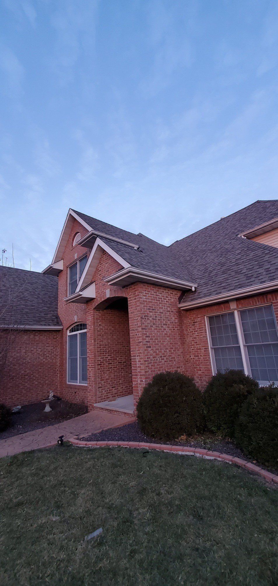 A large brick house with a gray roof and a large lawn in front of it.