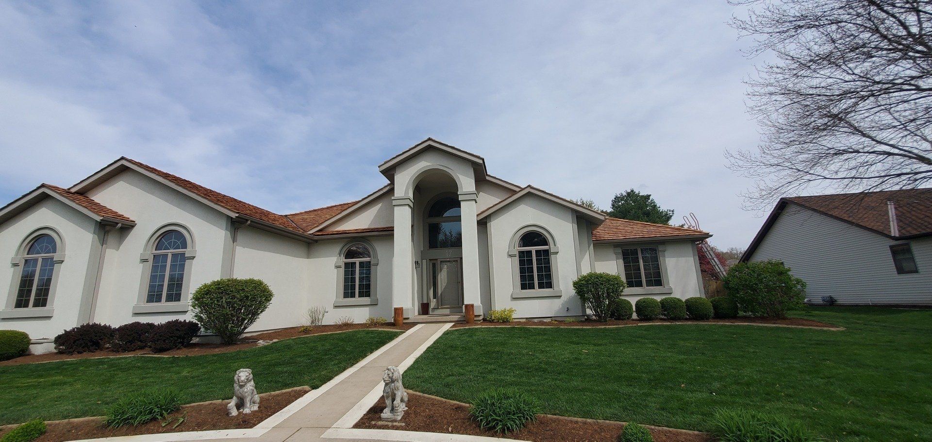 A large white house with a red tile roof is sitting on top of a lush green hillside.