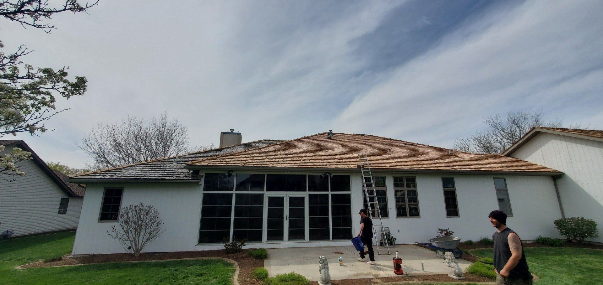 A man is standing in front of a white house with a roof that is being repaired.