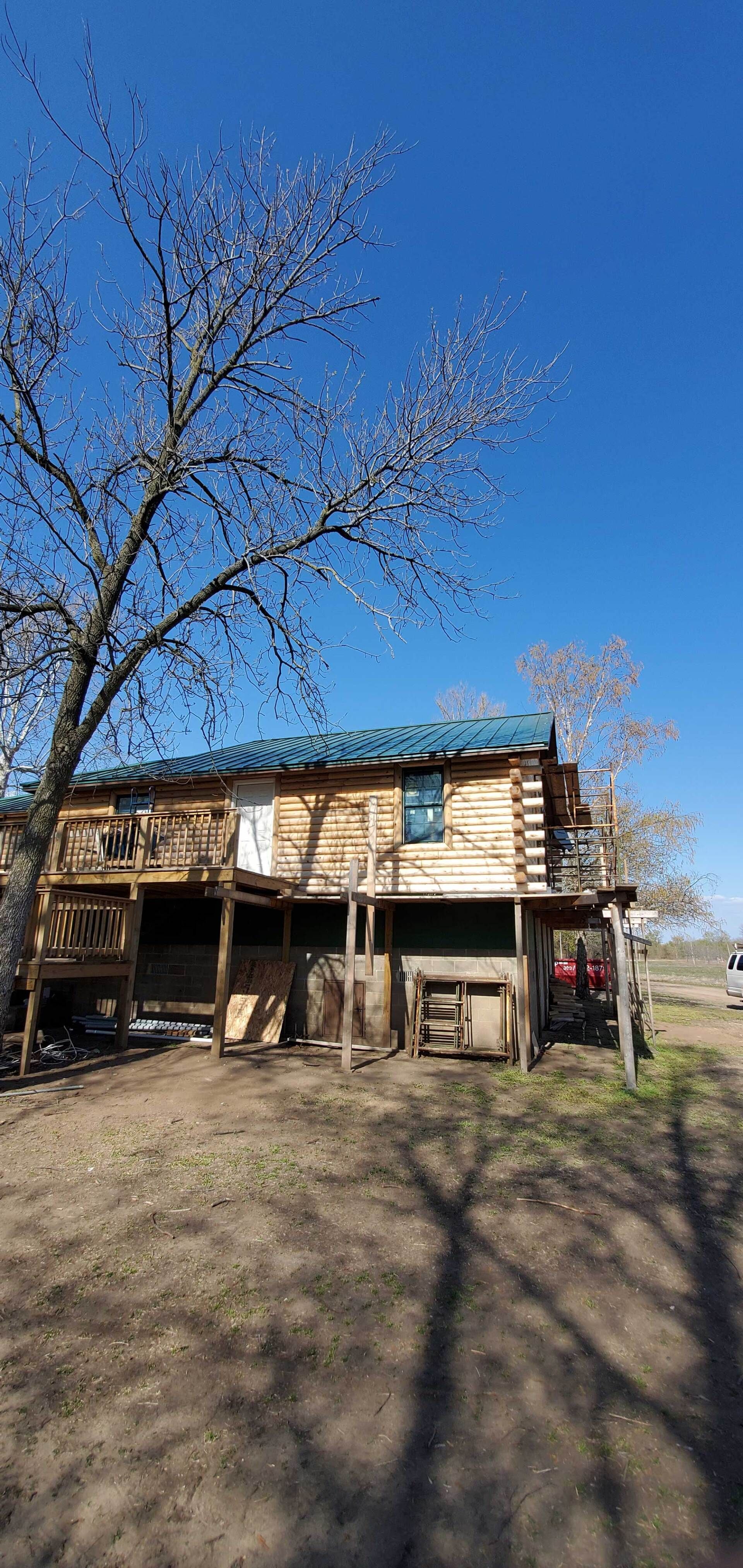 A small wooden house is sitting in the middle of a dirt field next to a tree.