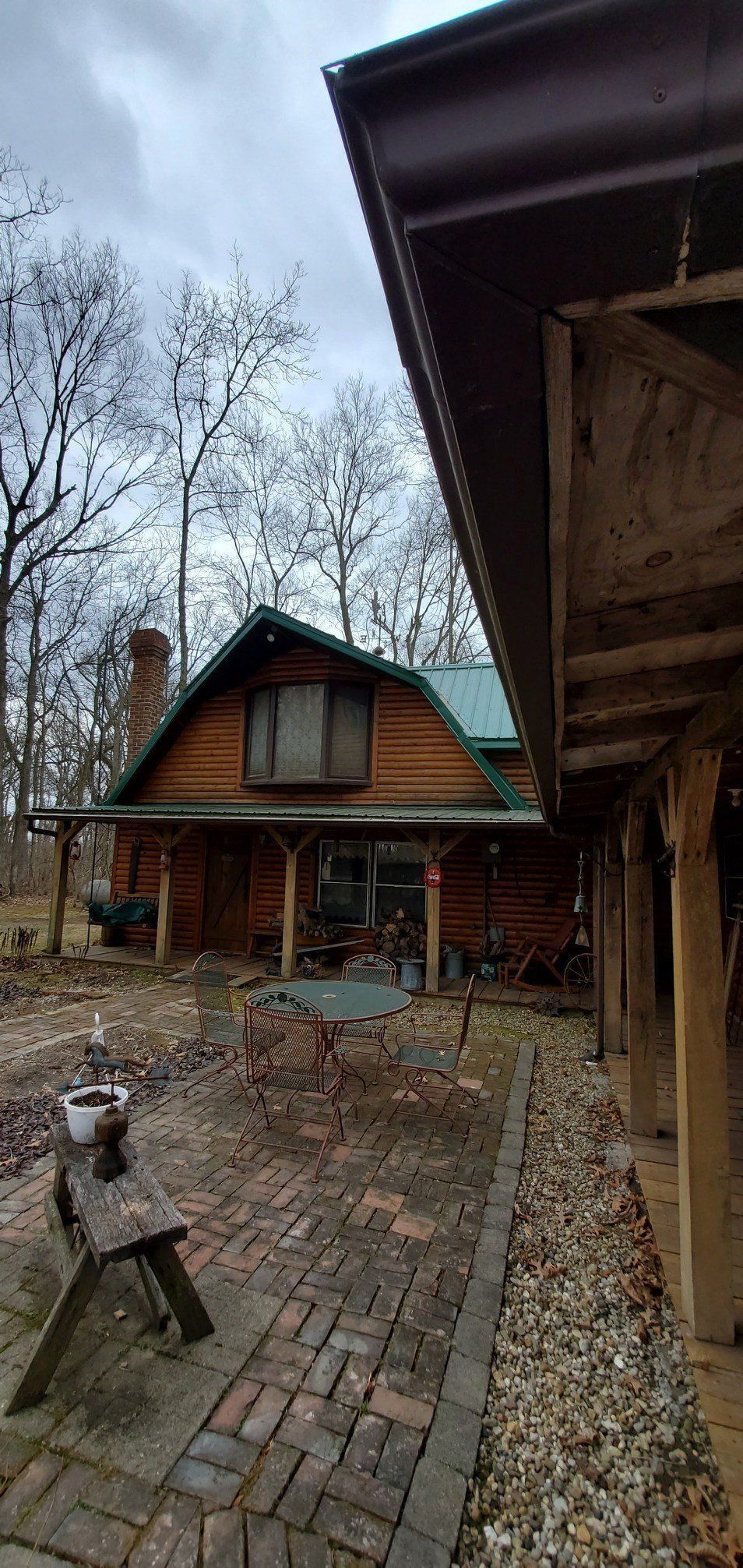 A log cabin with a green roof and a brick patio in front of it.