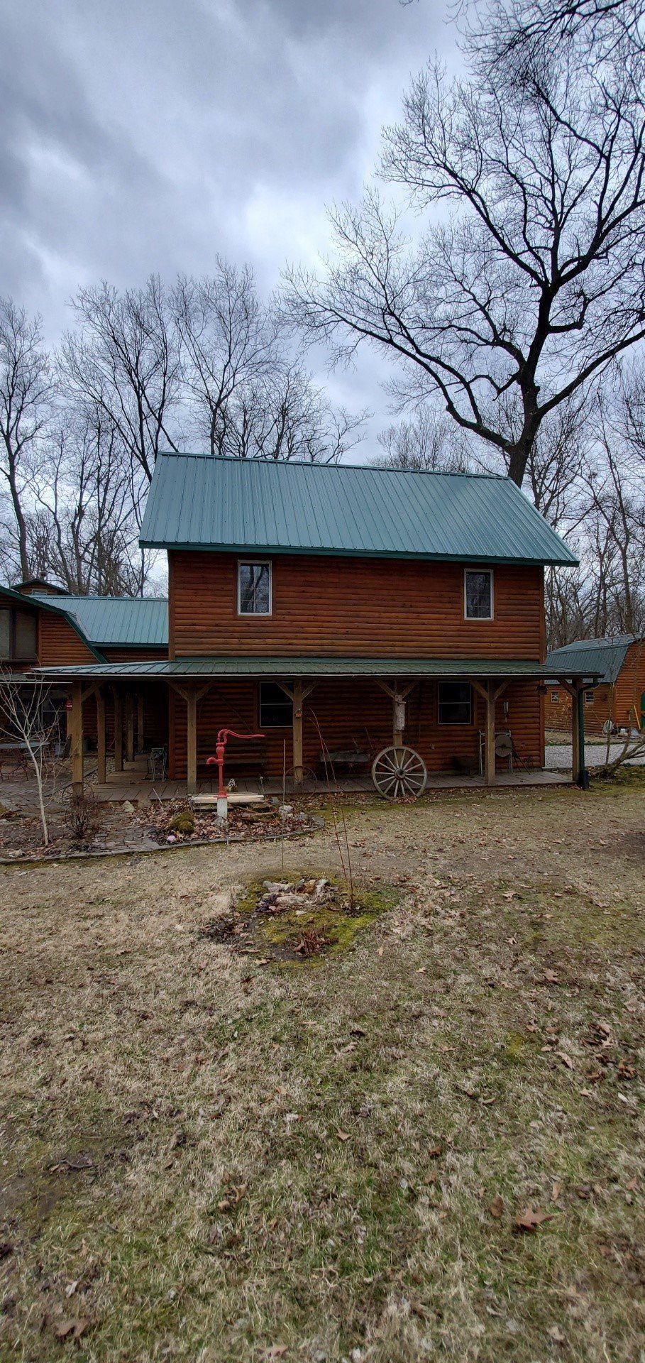 A log cabin with a green roof and a porch in the middle of a field.