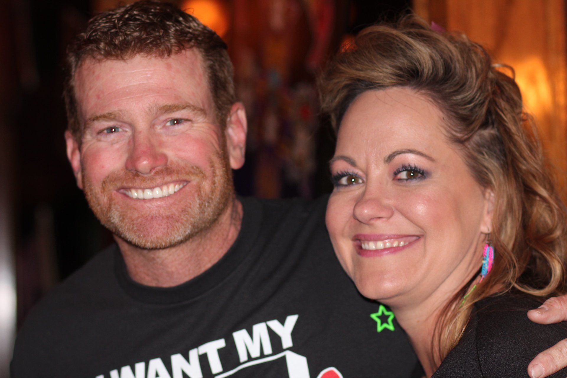 A man and a woman are posing for a picture and the man is wearing a shirt that says want my