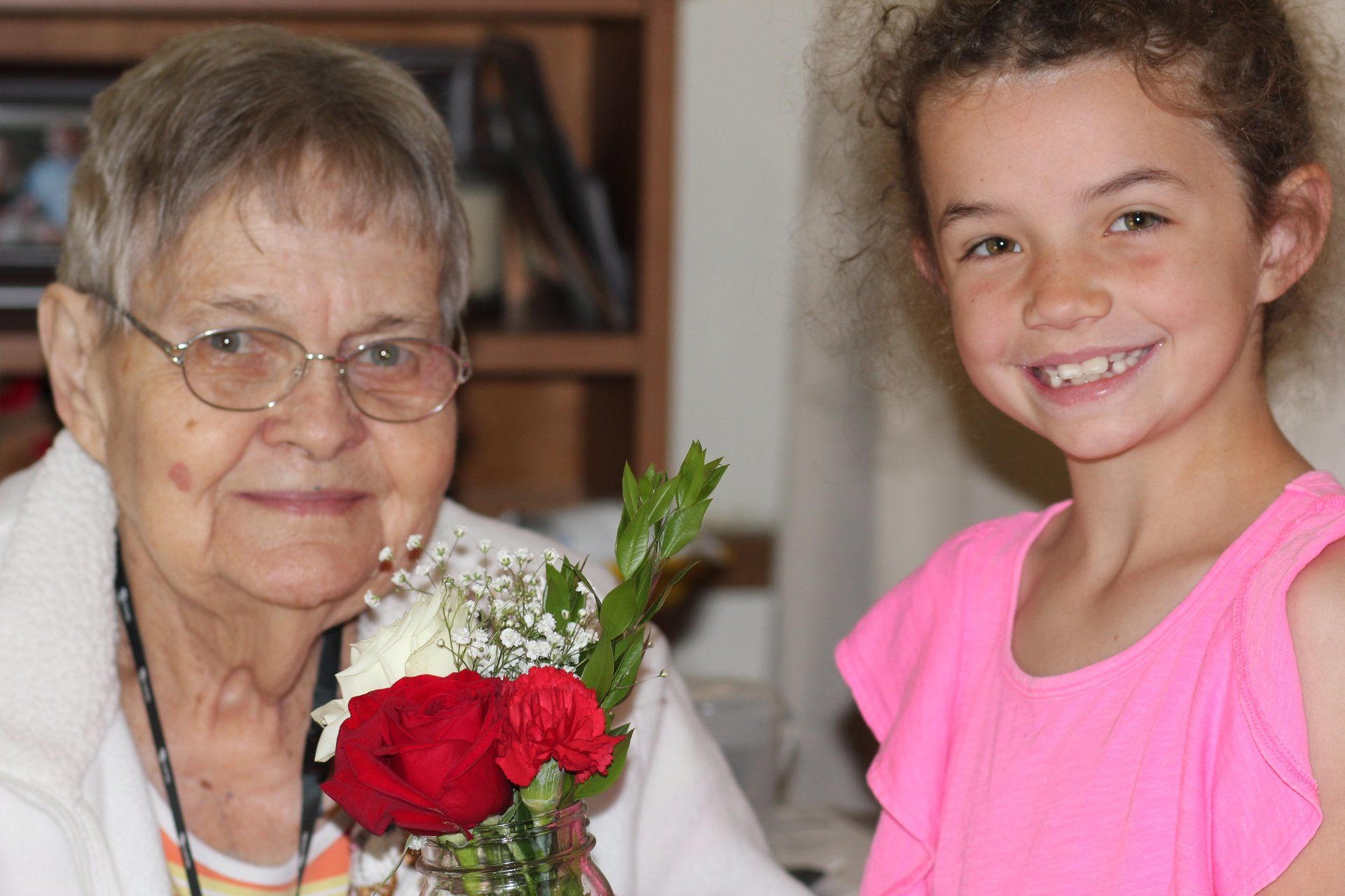 A little girl is holding a vase of flowers next to an older woman.