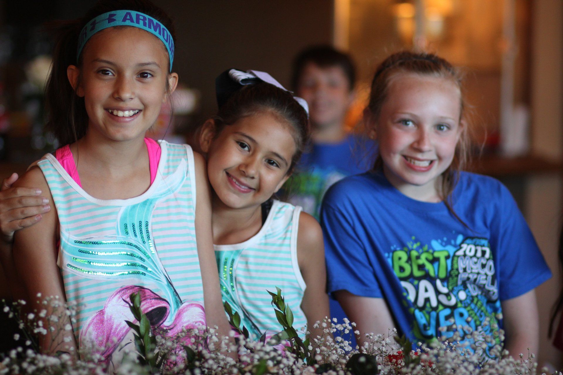 Three young girls are posing for a picture in front of flowers.