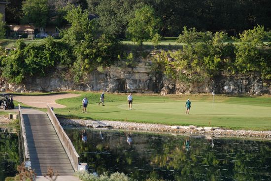 A green flag on a golf course with a rock wall in the background.