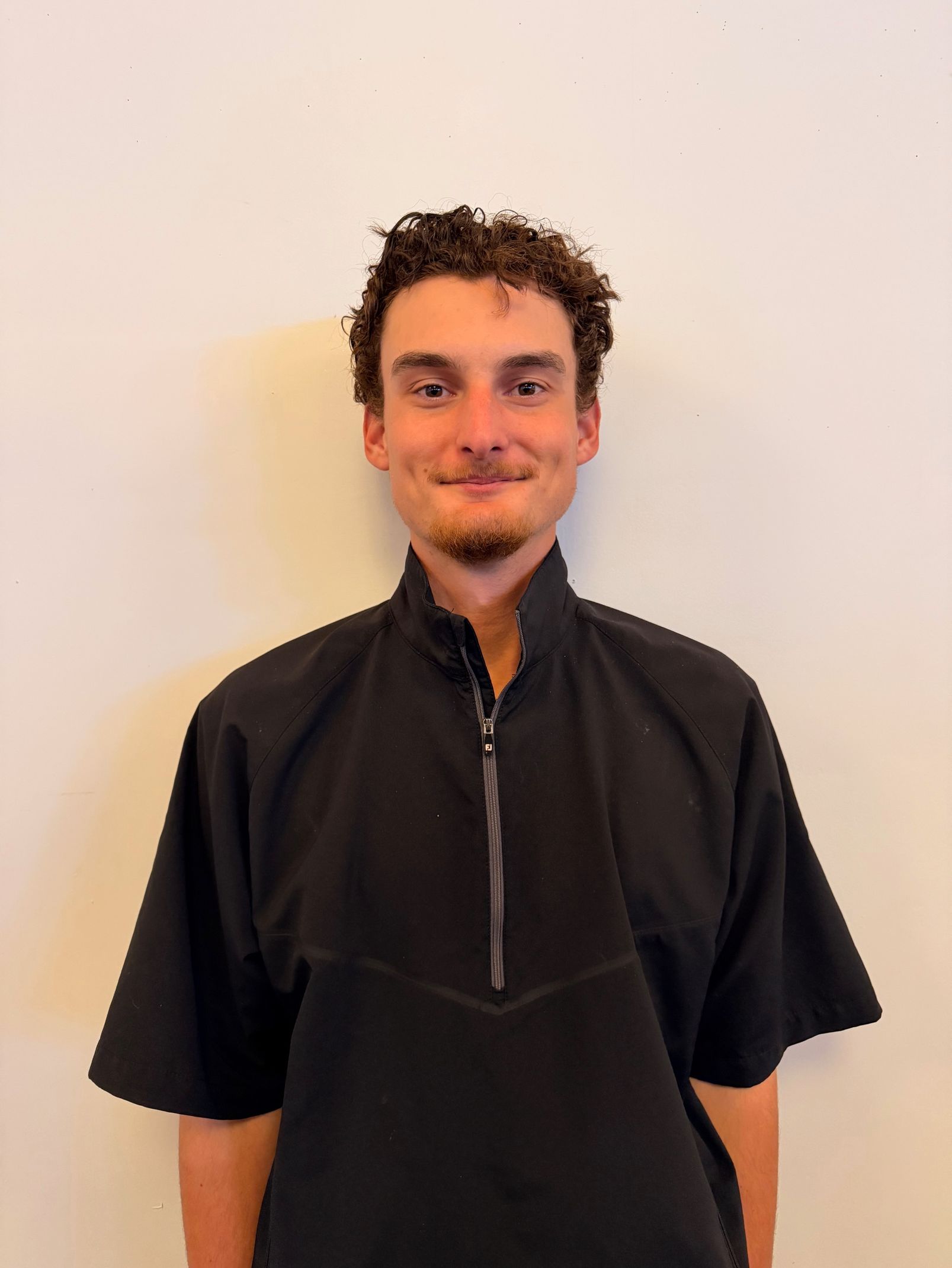 A man with a beard and mustache is wearing a black hoodie and smiling.