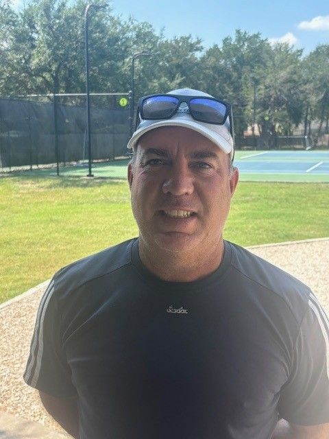 A man in a white shirt is smiling in front of a plant