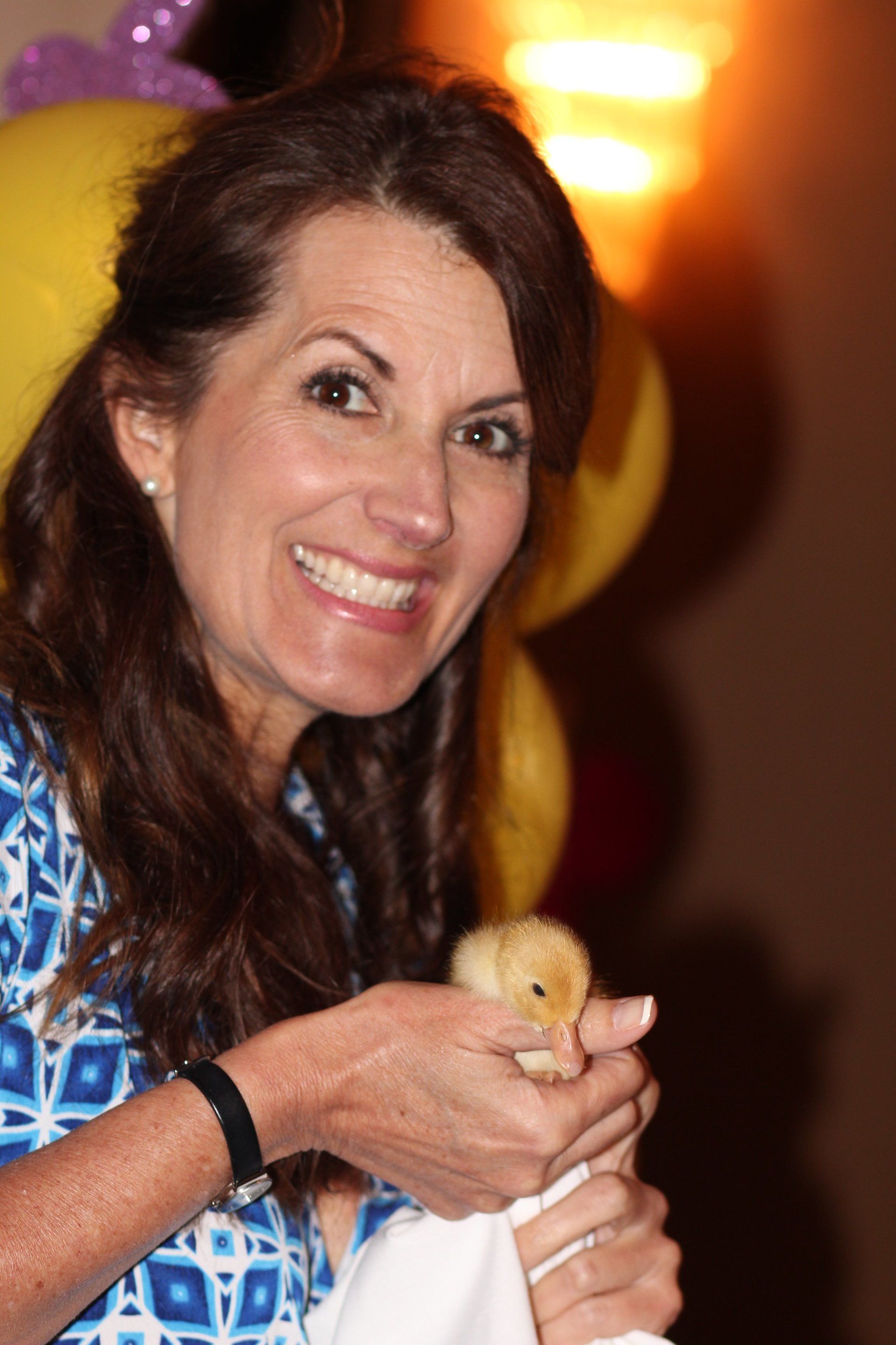 A woman is holding a small chick in her hands and smiling.