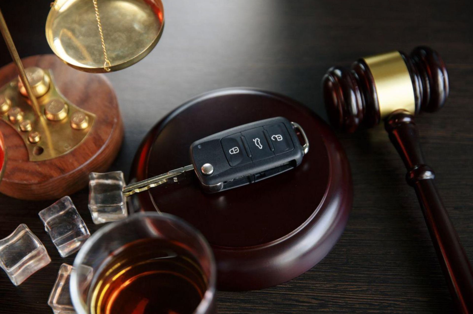 A car key is sitting on a wooden block next to a glass of alcohol.