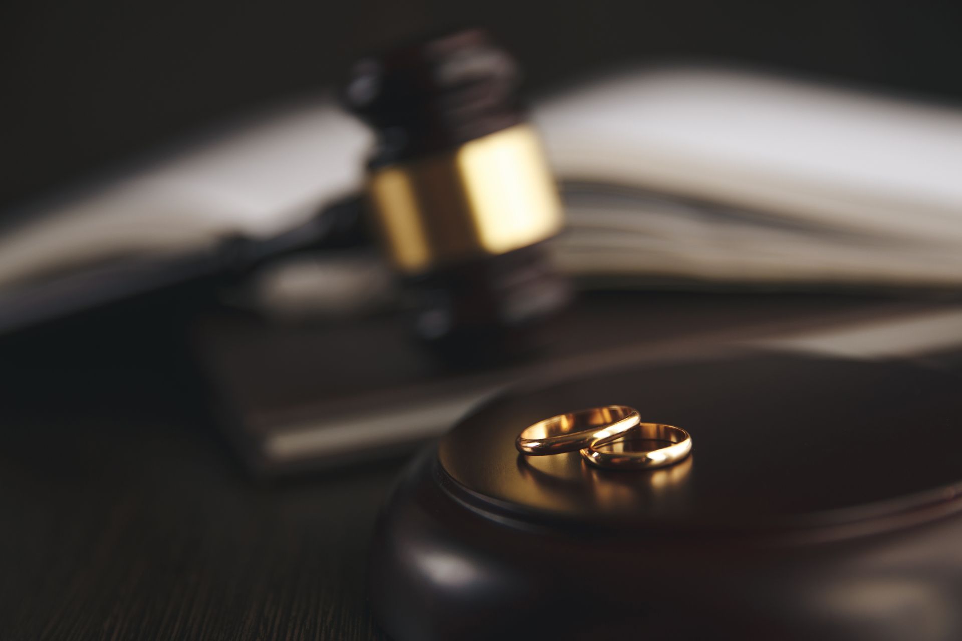 A pair of wedding rings sit on a wooden block in front of a judge's gavel.