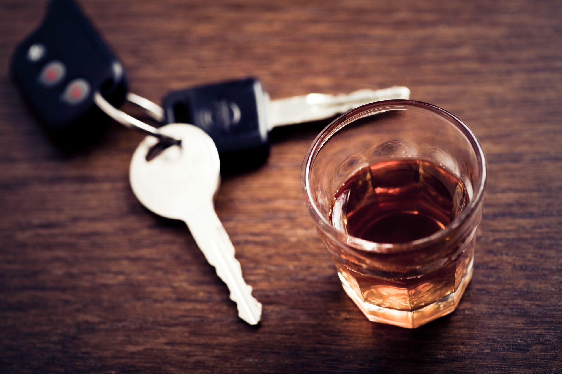 A car key and a shot glass of alcohol on a wooden table.