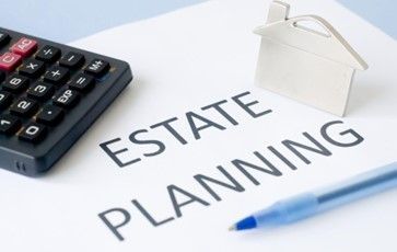 A calculator and a pen are on a piece of paper that says estate planning.