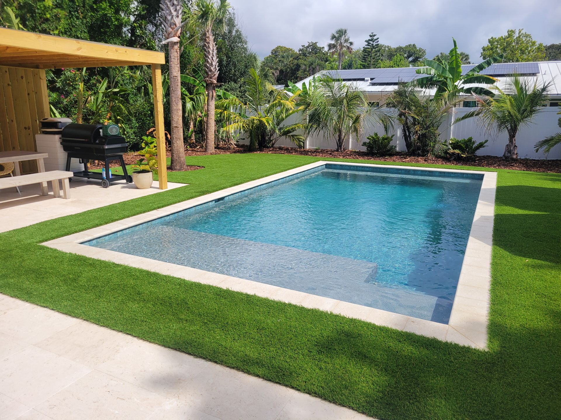 A large swimming pool is surrounded by lush green grass in a backyard.