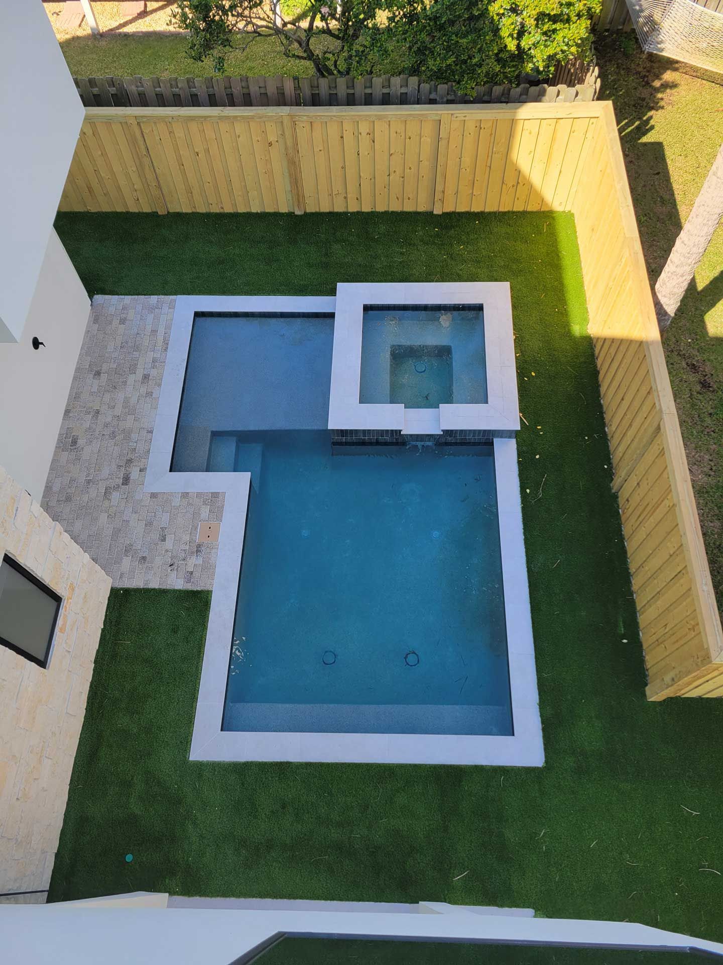 An aerial view of a swimming pool in a backyard with a wooden fence.
