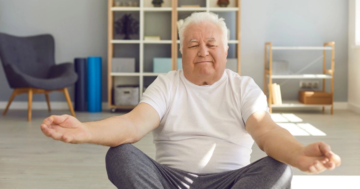 Person sitting cross-legged on a living room floor, meditating with eyes closed and arms resting on knees.