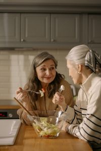 Two people in a kitchen talking while preparing a salad at the counter.