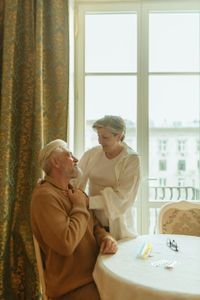 Two people sharing a warm conversation beside a sunlit window and round table
