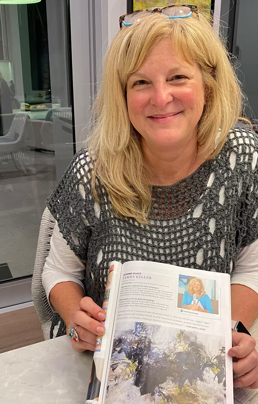 Woman with blonde hair wearing glasses and gray sweater, holding open book with photograph.