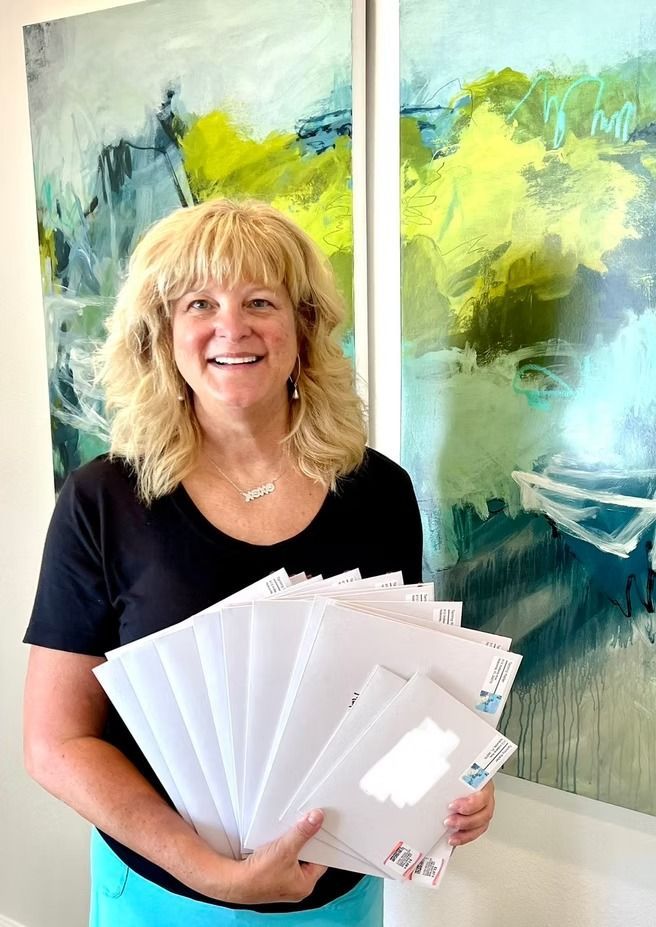 Woman holding a stack of envelopes, smiling. She is in front of abstract art.