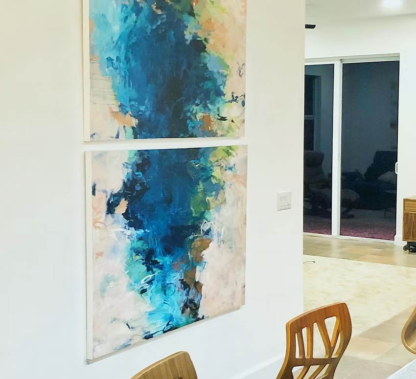 Two abstract blue and white paintings hung on a white wall in a dining area.