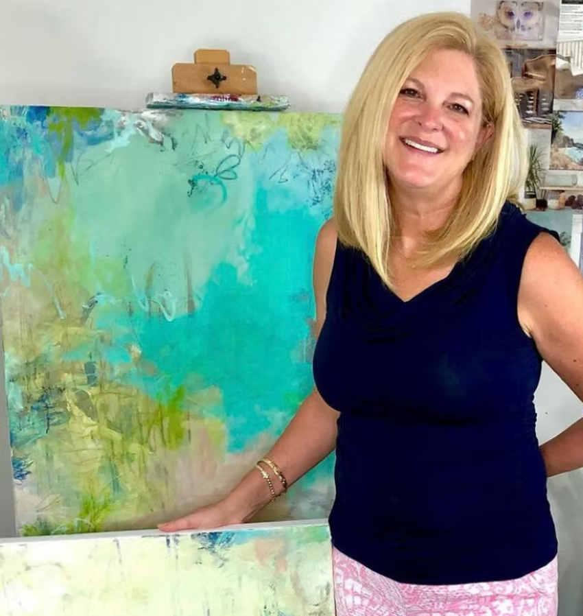 Woman smiling, posing next to abstract painting with teal and yellow hues.