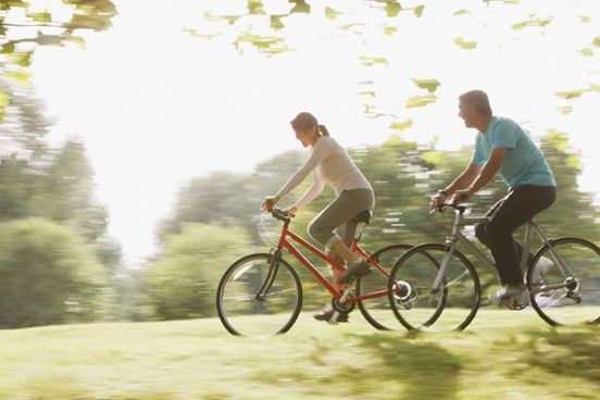 A man and a woman are riding bicycles in a park.