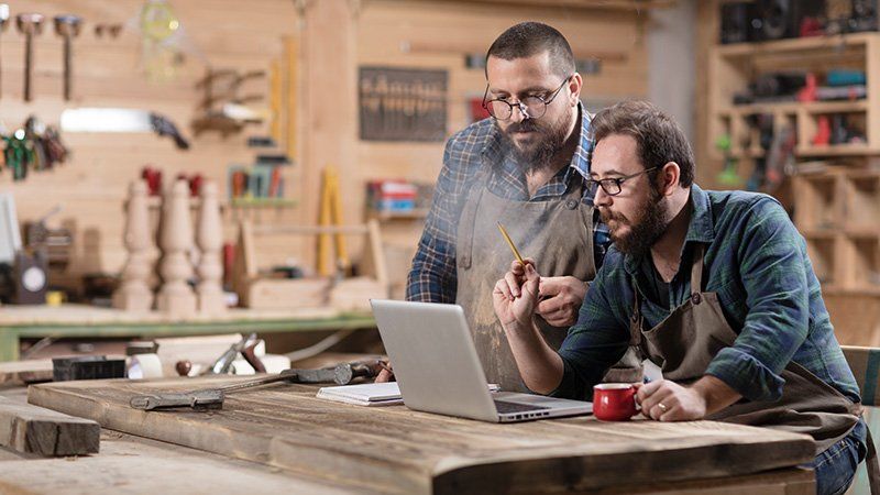 Two men in a workshop look over a laptop