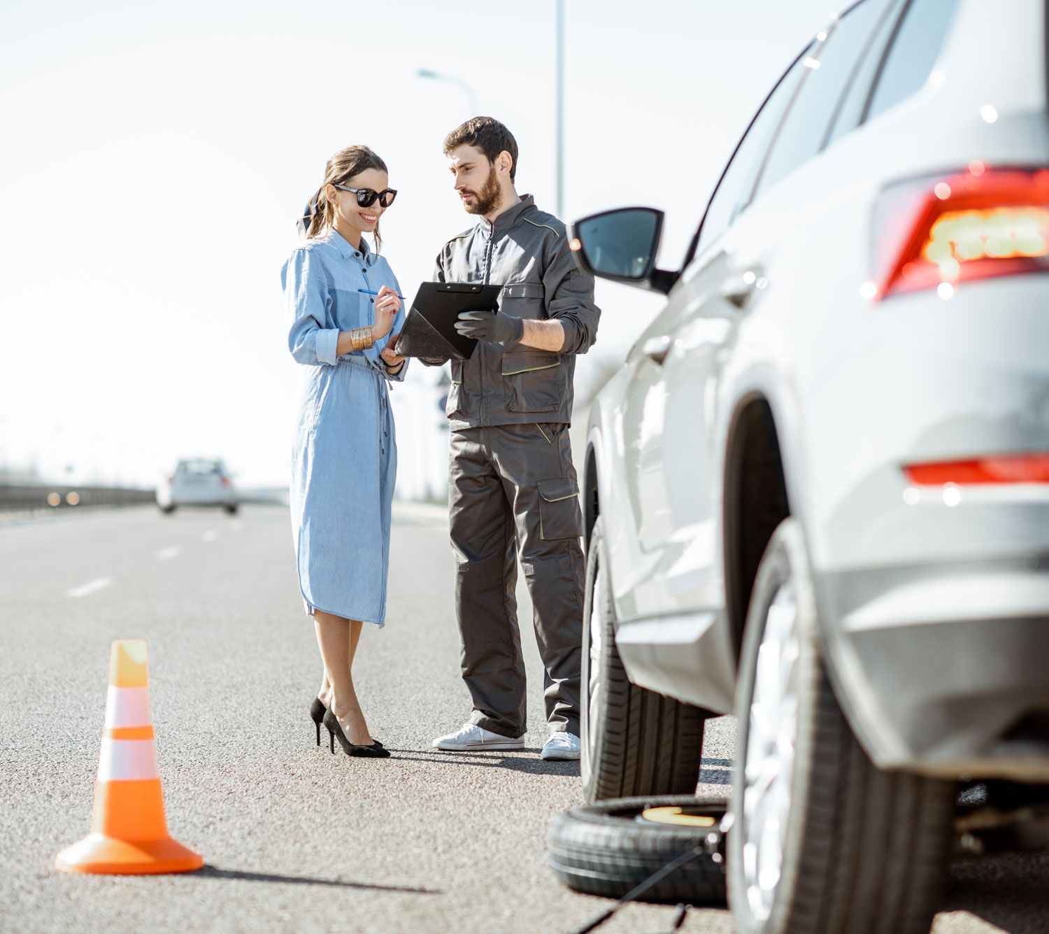 road assistance worker signing document with woman near the broken car on highway