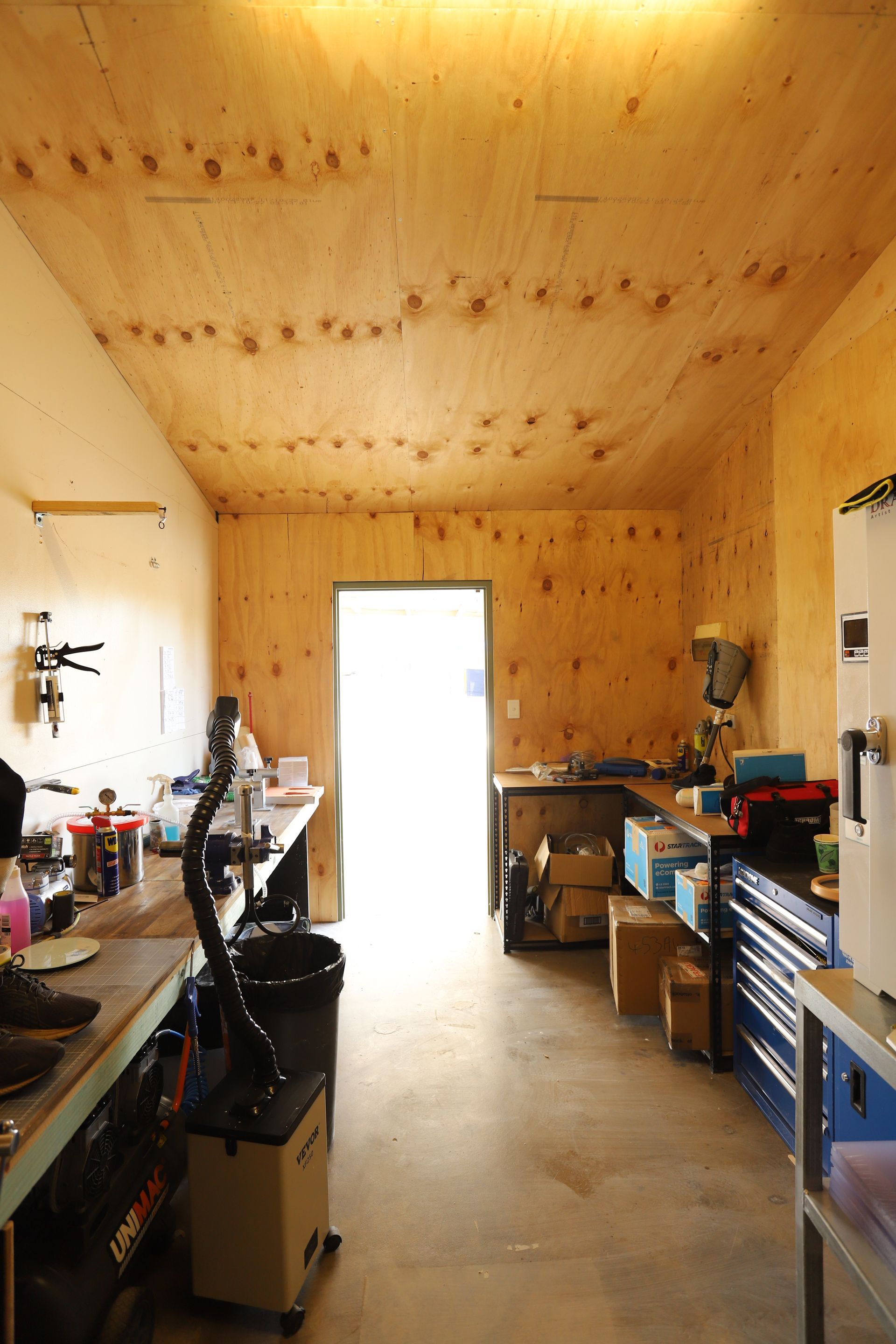 Workshop interior with wooden walls and ceiling. A bright doorway is visible at the end of the room.