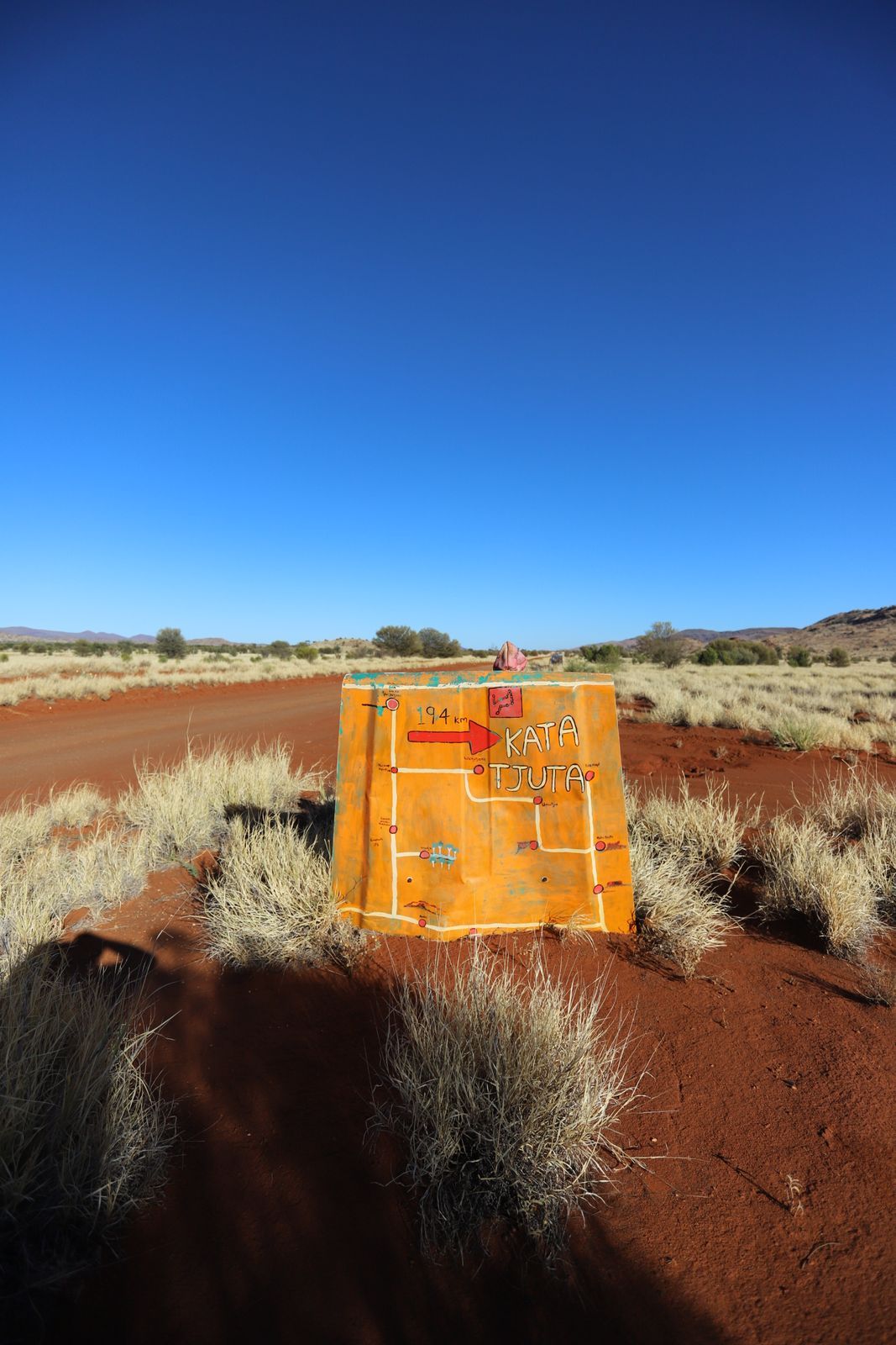 Yellow directional sign with red arrow in Australian outback; clear blue sky.