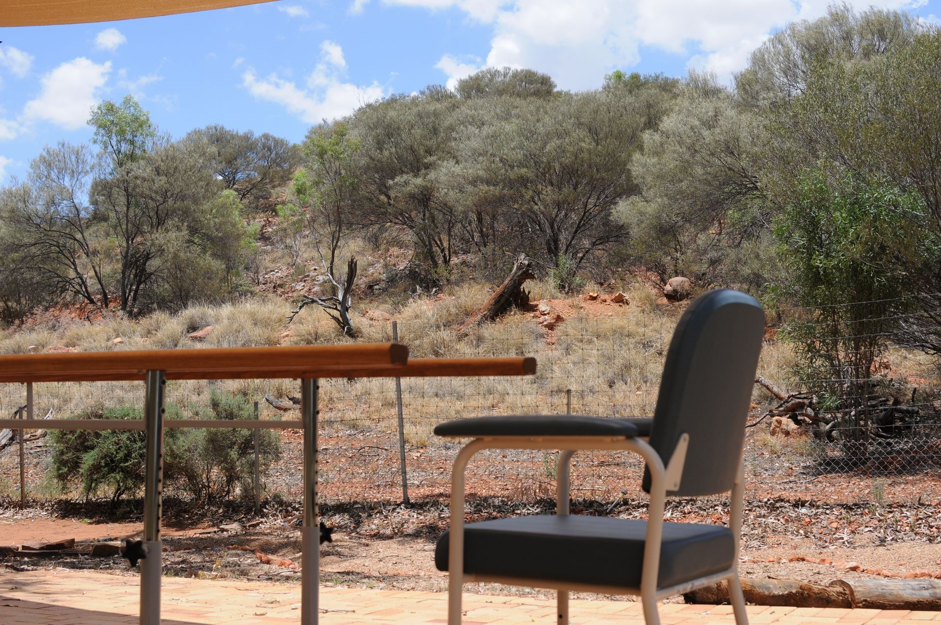 A chair and table on a patio, overlooking a hillside with trees. Bush Steps mobility garden