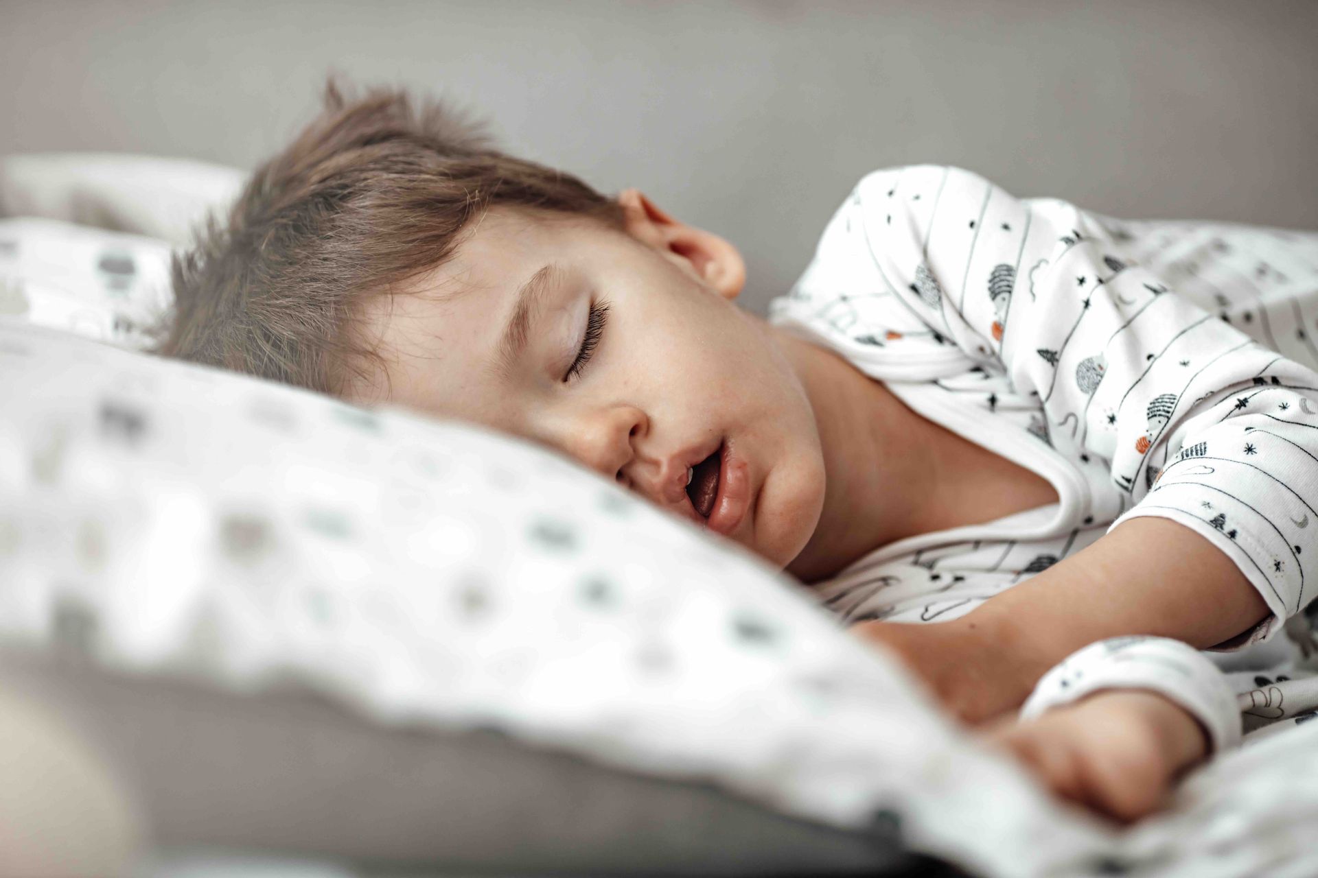 Sleeping child lying on a white bed with patterned sheets