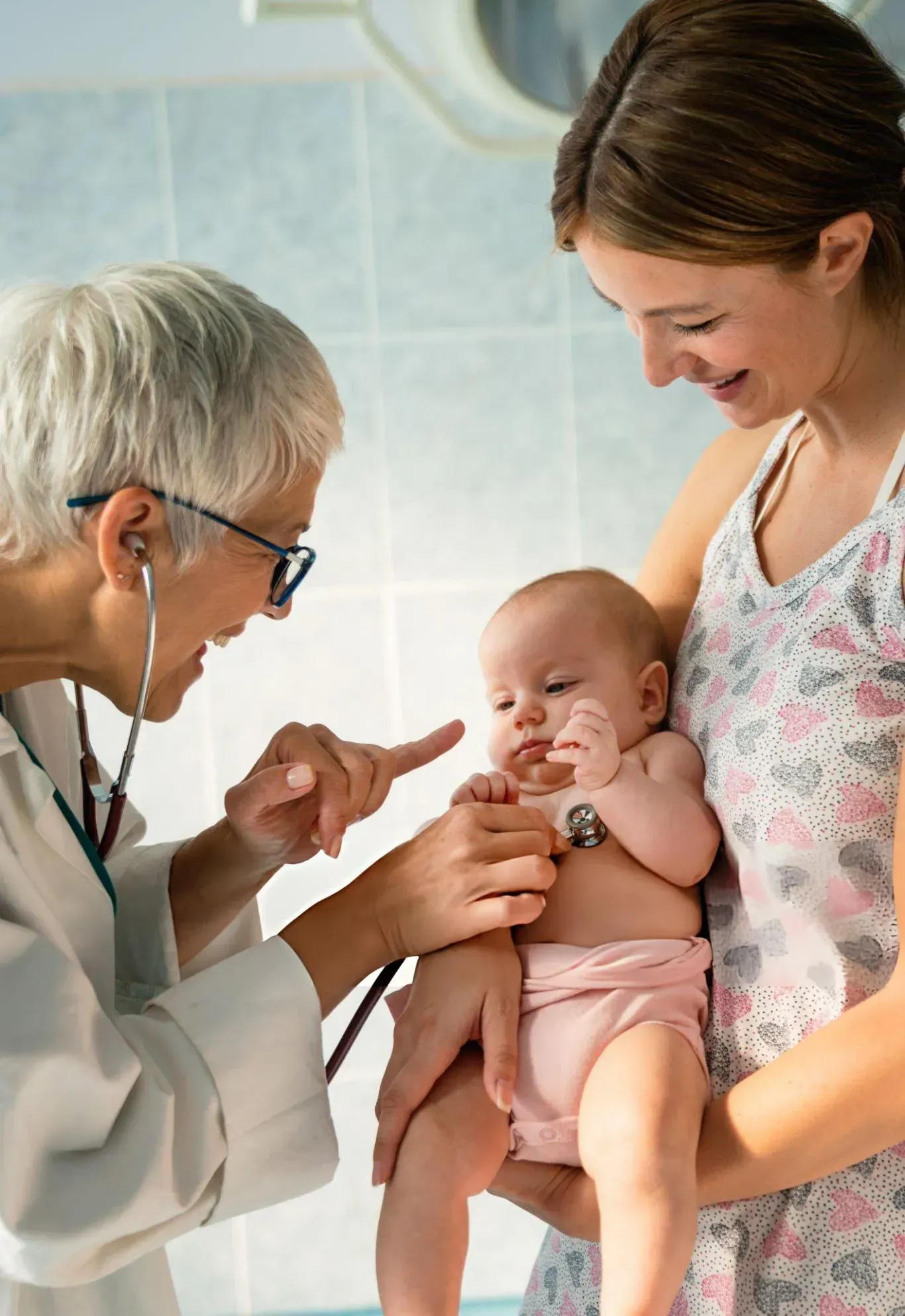 A woman is holding a baby while a doctor examines it with a stethoscope.