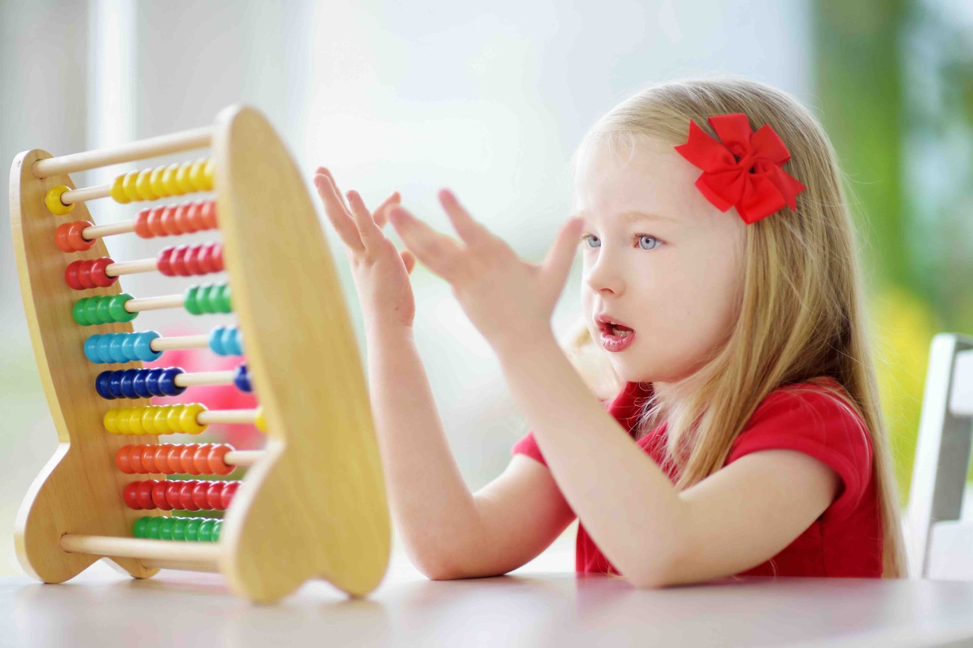 A little girl is sitting at a table playing with an abacus.