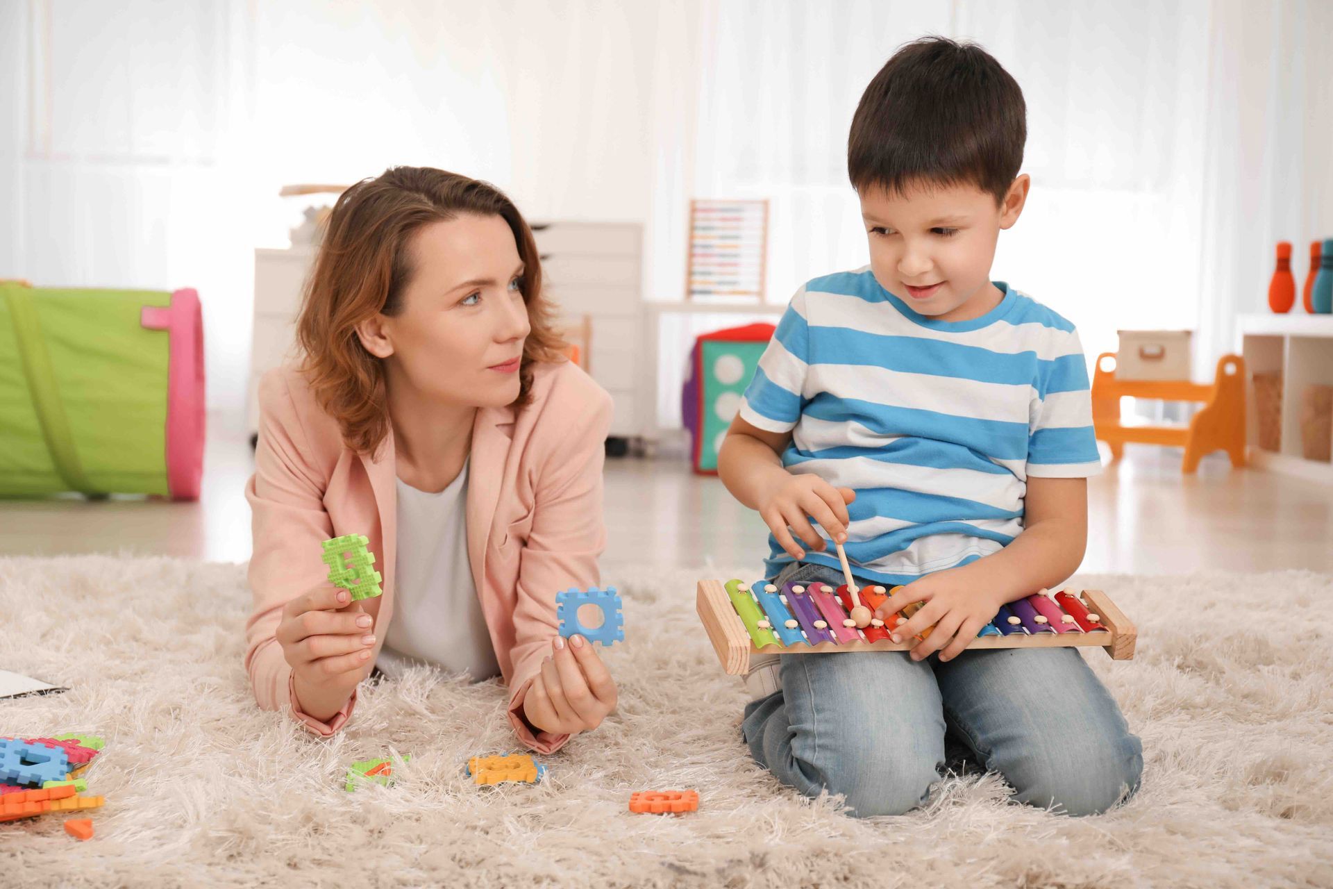 A woman and a child are playing with toys on the floor.