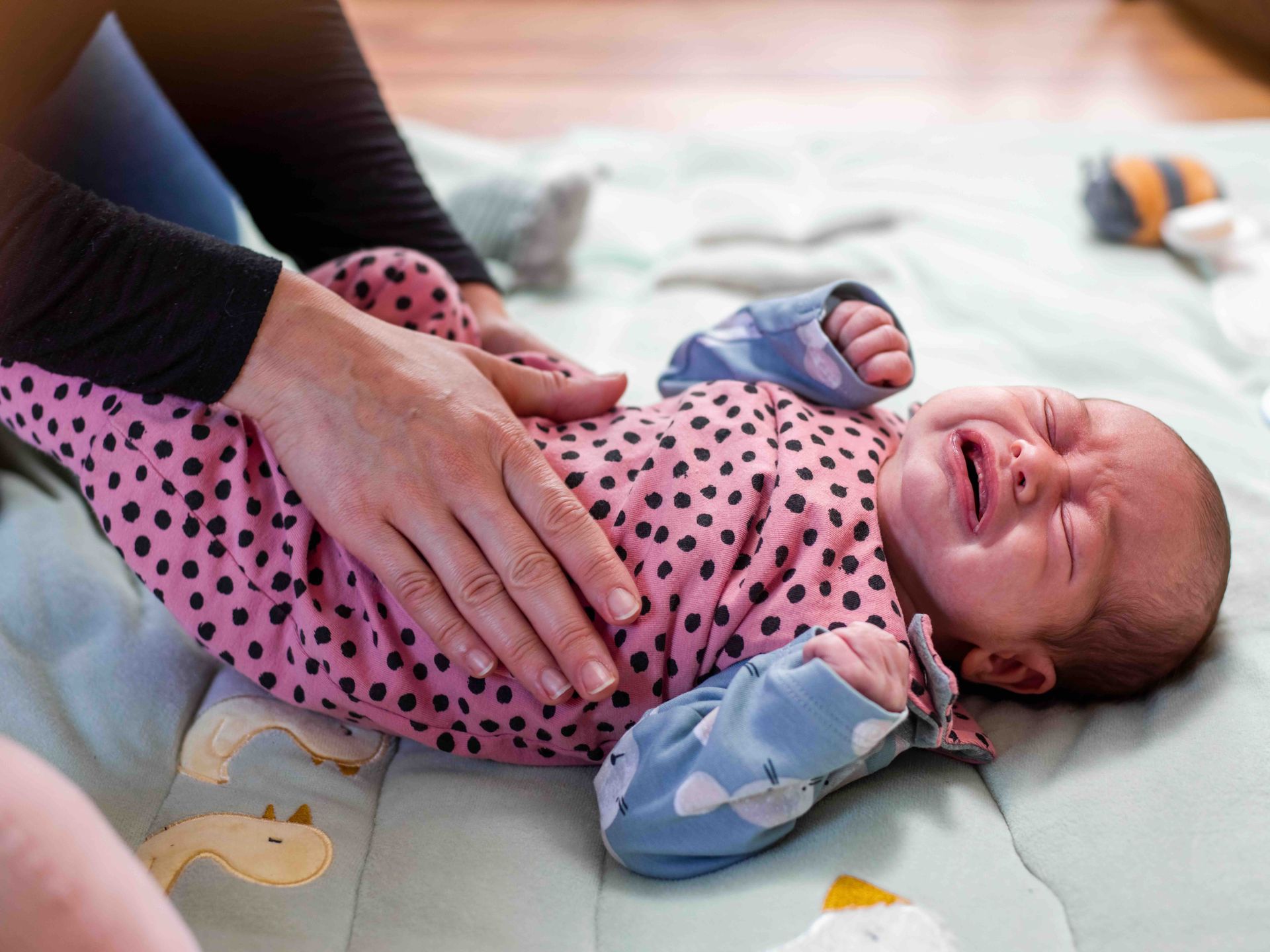 A woman is comforting a crying baby on a blanket on the floor.