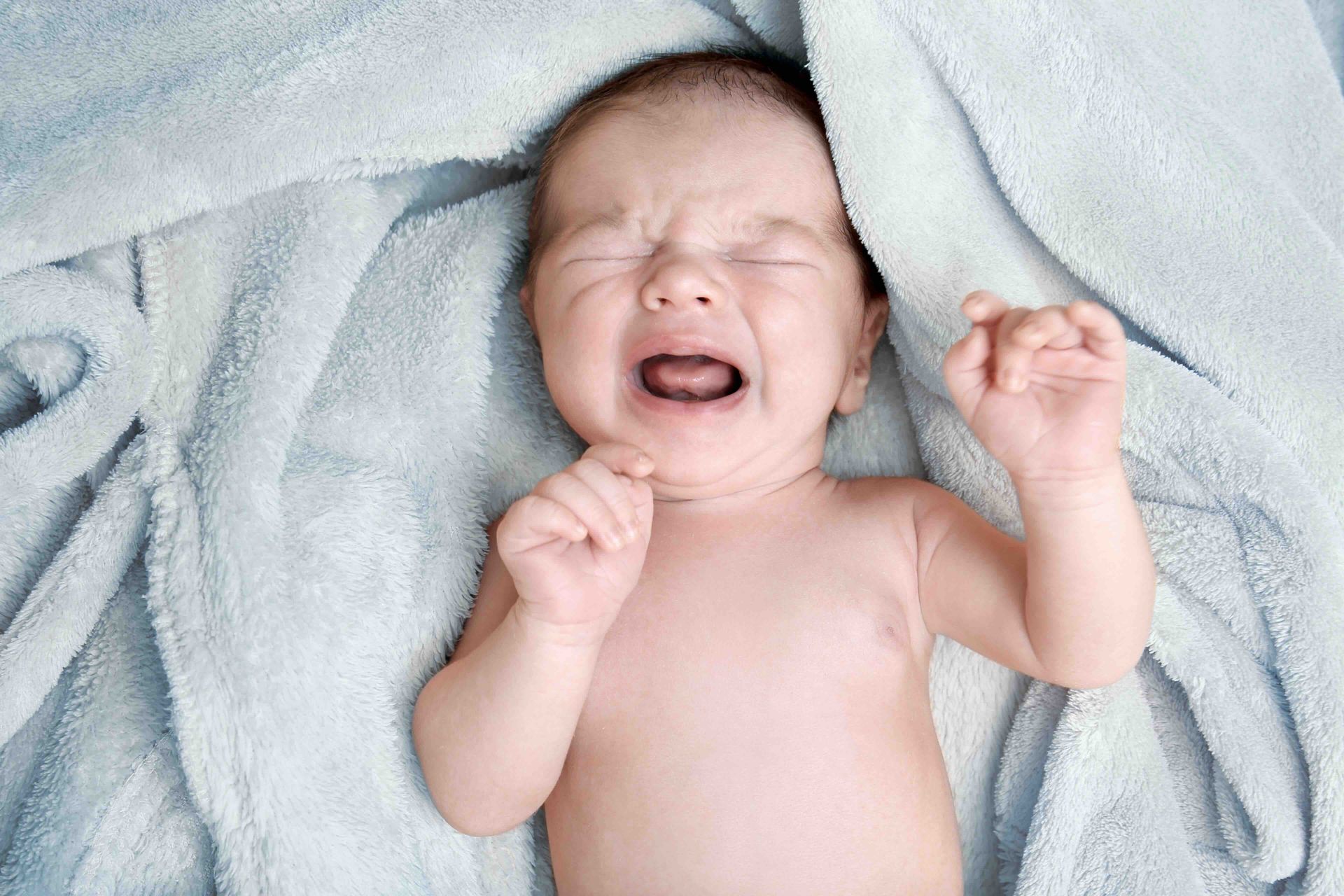 A baby is crying while laying on a blanket.