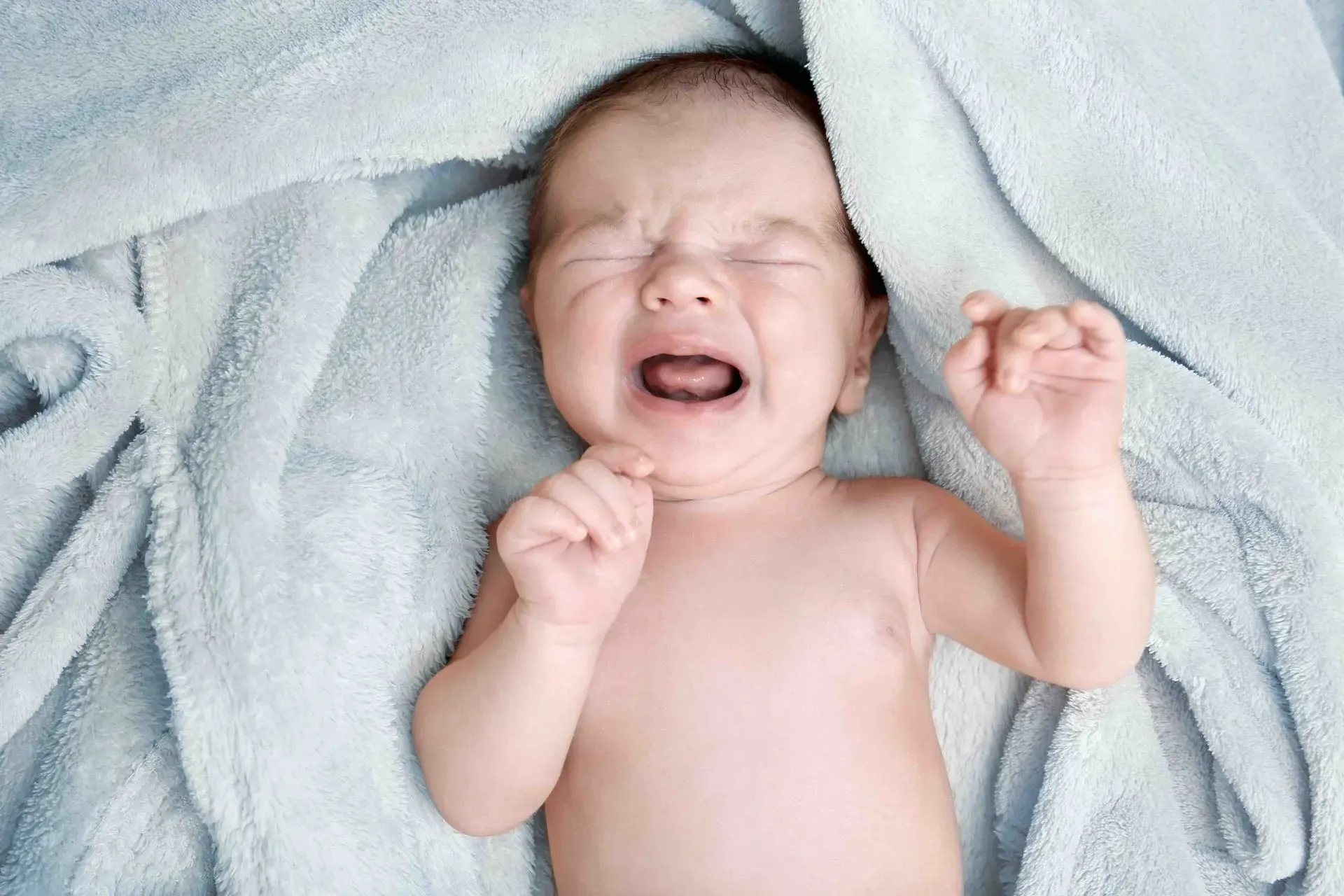 A baby is crying while laying on a blanket.