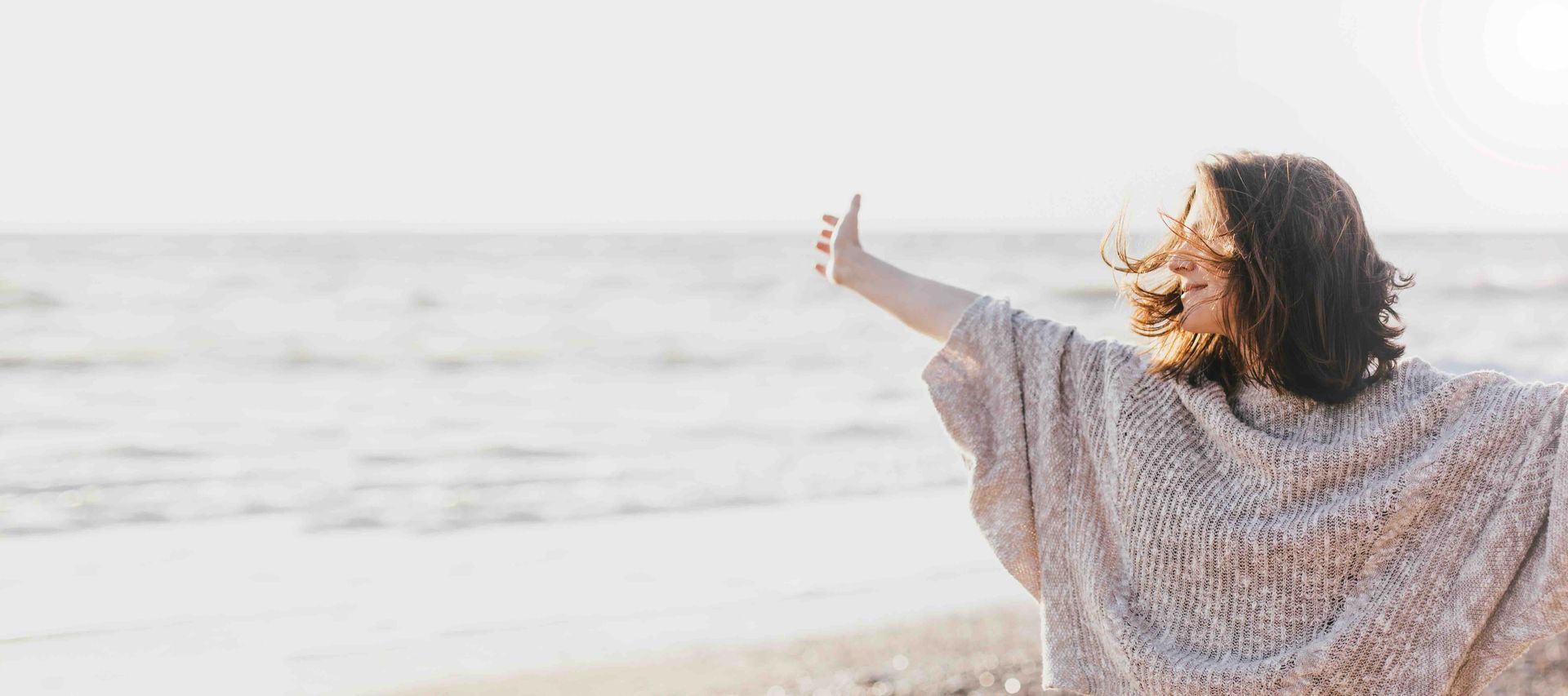 A woman with her arms spread open with a smile on her face is standing on a beach.