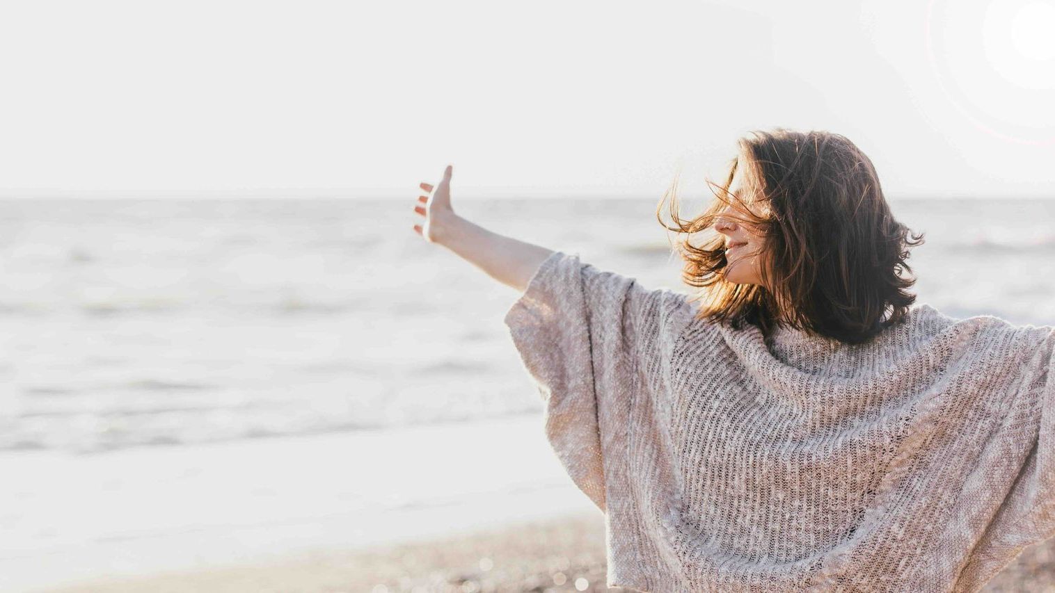 A woman with her arms spread open with a smile on her face is standing on a beach.