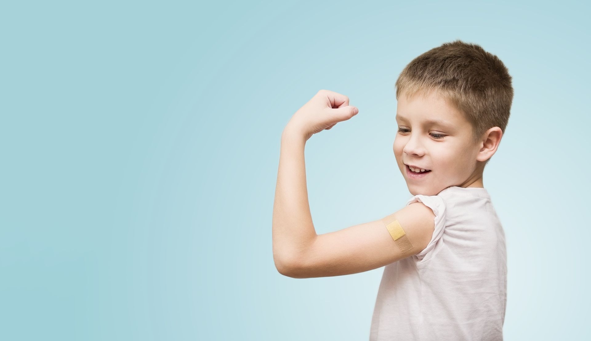 A young boy with a bandage on his arm is flexing his muscles.