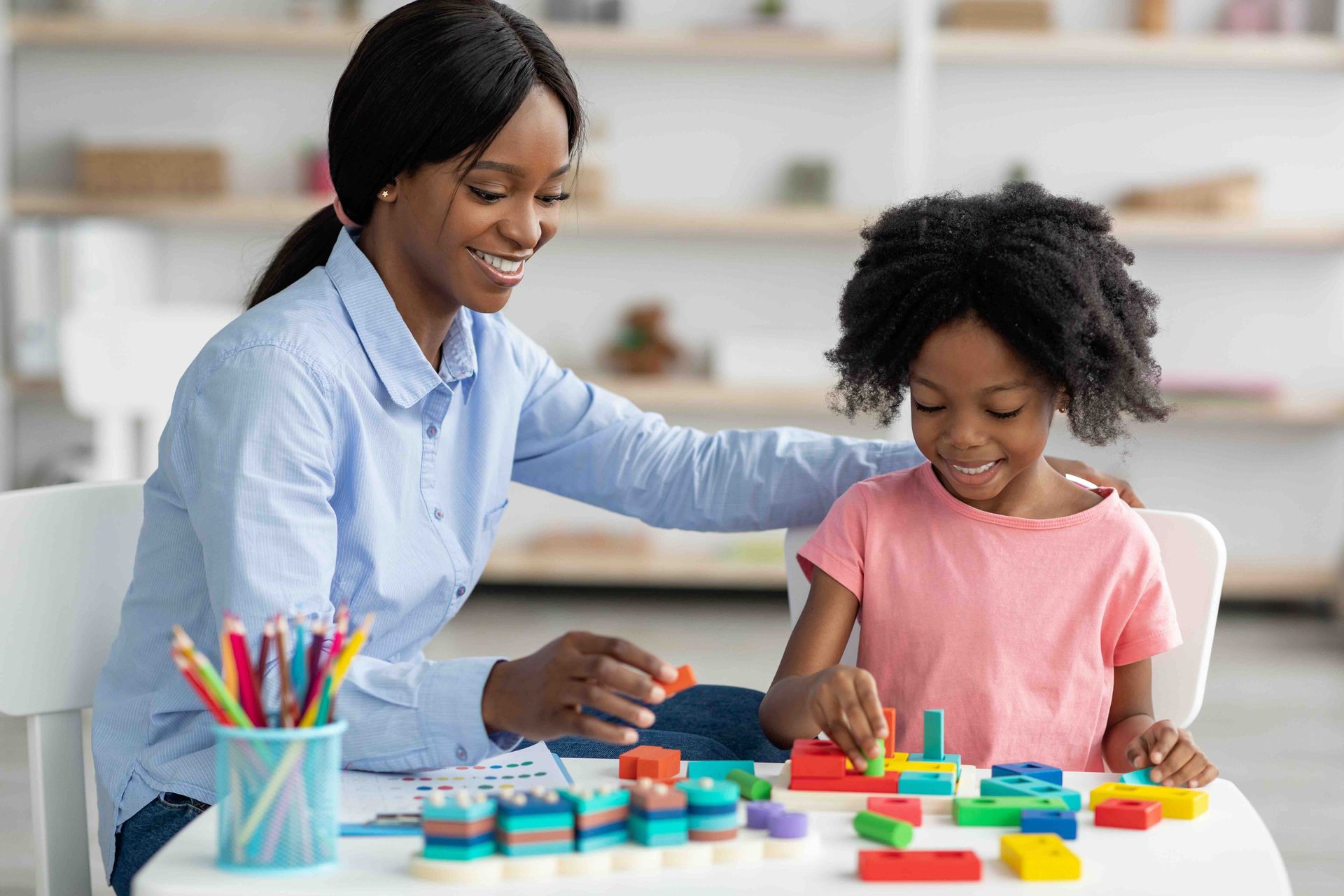 A woman and a little girl are playing with blocks at a table.