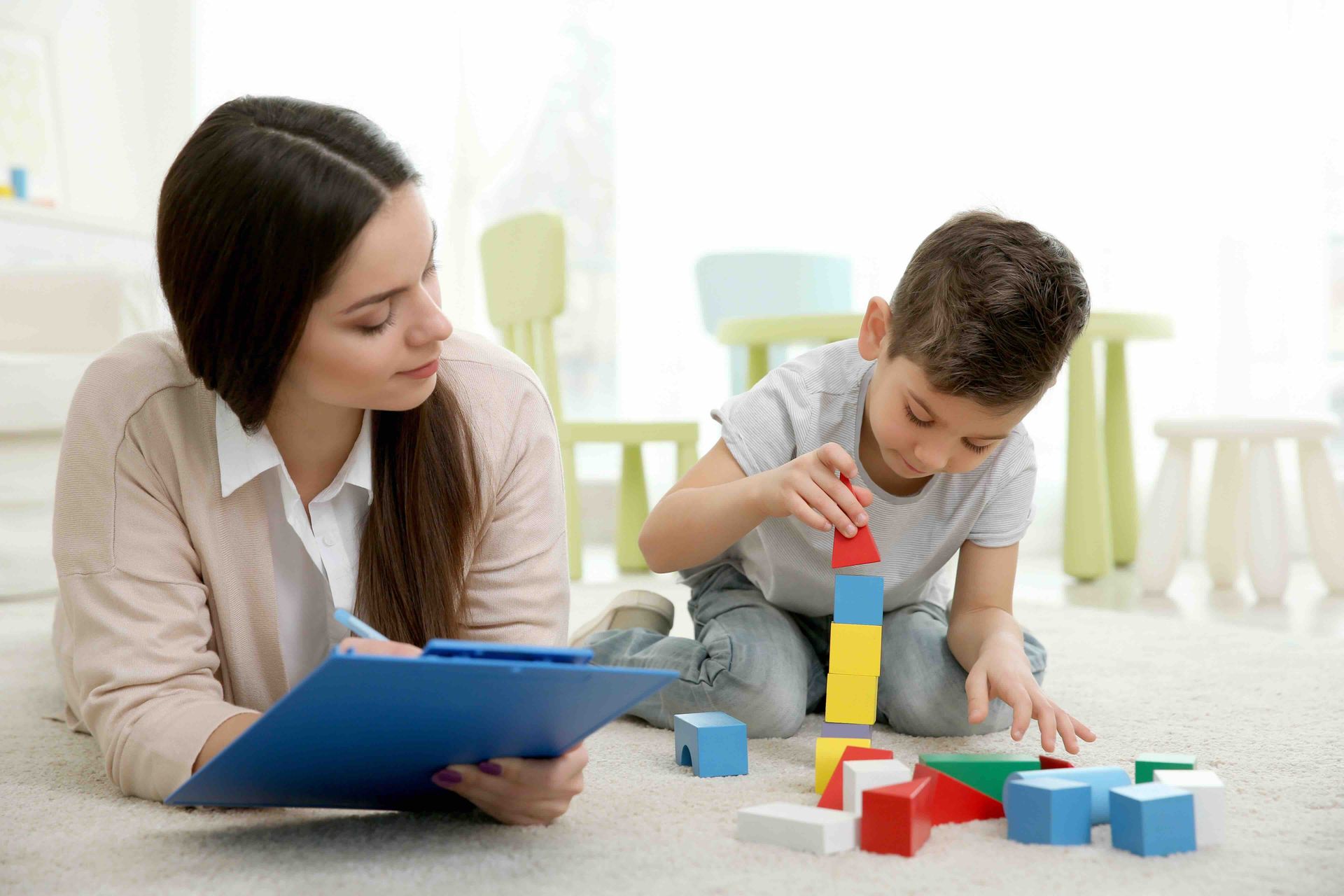 A woman is sitting on the floor with a child playing with blocks.