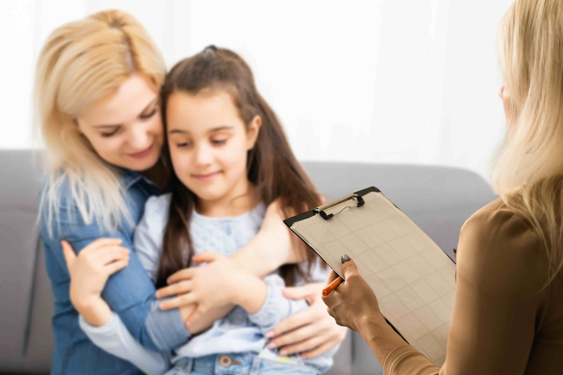 A mother and daughter are sitting on a couch talking to a female psychologist.