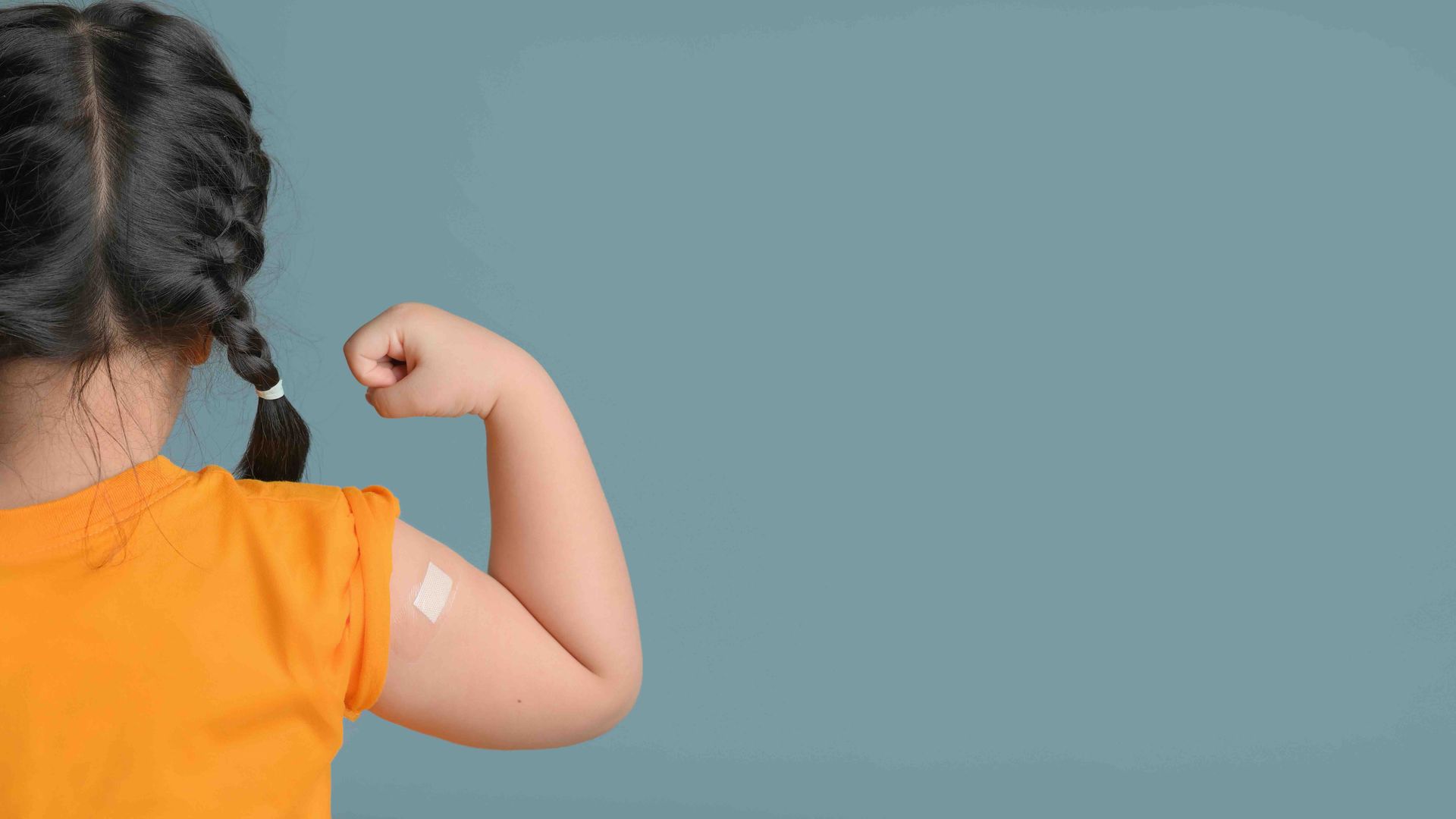 A little girl with a bandage on her arm is flexing her muscles.