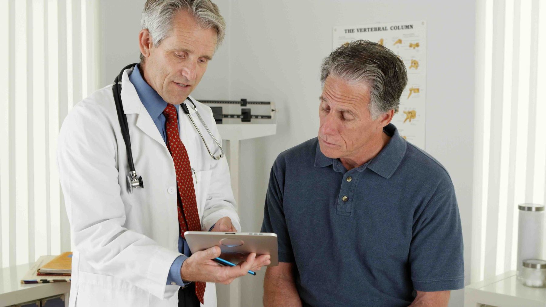 a doctor is talking to a male patient while looking at a tablet.