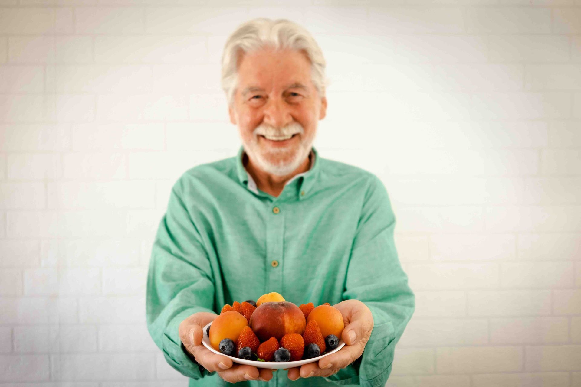 An elderly man is holding a plate of fruit in his hands.