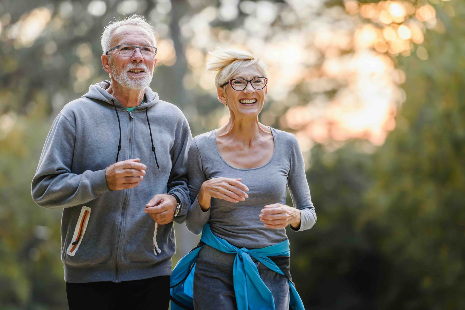 An elderly couple is jogging together in a park.